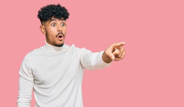 Kış süveteri giymiş genç bir Arap. Parmağıyla işaret ediyor. İleriyi işaret ediyor. 