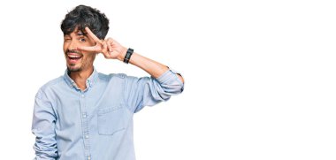 Gündelik kıyafetler giyen genç İspanyol adam barış sembolü yapıyor. Yüzünde parmaklar, gülümseyerek zaferi gösteriyor. 