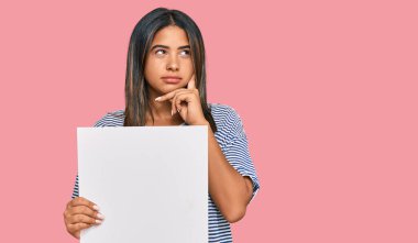 Boş afiş taşıyan genç Latin kız. Ciddi bir yüz. Soru soran eli çeneli, kafa karıştırıcı bir fikir. 