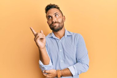 Sakallı, sıradan giyinmiş, mutlu gülümseyen, eli ve parmağı yanda olan yakışıklı bir adam. 