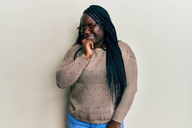 Örgülü, sıradan kıyafetler ve gözlüklü genç siyahi kadın kameraya kendinden emin bakıyor kolları çapraz ve çenesi açık gülümsüyor. Olumlu düşünmek. 