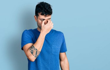 Gündelik tişört giyen genç İspanyol adam yorgun burnu ve gözleri ovuşturup yorgunluk ve baş ağrısı hissediyor. Stres ve hüsran kavramı. 