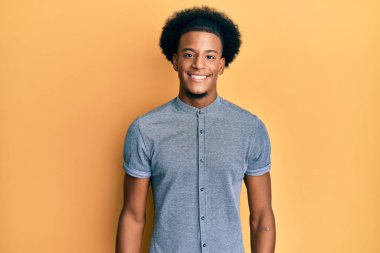 Afro saçlı, mutlu ve havalı bir gülümsemesi olan sıradan kıyafetler giyen Afro-Amerikan bir adam. şanslı kişi. 