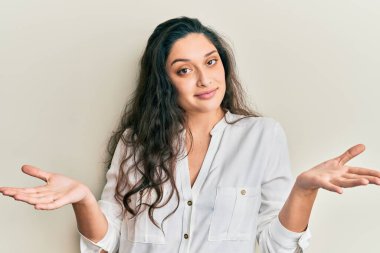 Güzel bir ortadoğulu kadın, gündelik kıyafetler giyiyor, elleri ve kolları havada, kafası karışmış bir ifade takınıyor. şüphe kavramı. 