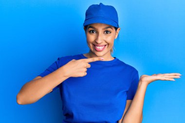 Güzel esmer kadın teslimat üniforması giyiyor. Kameraya hayret ediyor ve gülümsüyor.. 