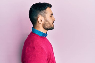 Latin kökenli genç bir adam günlük giysiler giyiyor, rahat bir görünüm takınıyor, doğal bir yüz ifadesi ve kendinden emin bir gülümsemeyle poz veriyor.. 