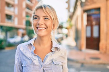 Genç sarışın kadın gülümseyerek şehirde mutlu mesut yürüyor..