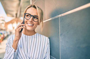 Genç sarışın iş kadını şehirde akıllı telefon kullanarak mutlu bir şekilde gülümsüyor..