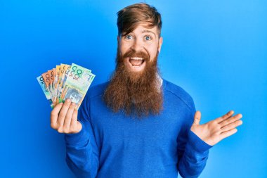 Genç İrlandalı kızıl saçlı adam Avustralya dolarlarını tutuyor başarıyı mutlu bir gülümsemeyle kutluyor ve kazanan el kaldırarak ifade ediyor 