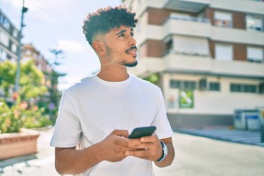 Genç Arap adam şehirde akıllı telefon kullanarak mutlu bir şekilde gülümsüyor..