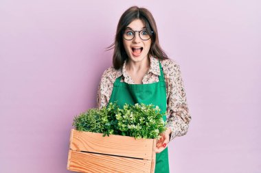 Genç, beyaz, bahçıvan önlüğü giymiş genç bir kız elinde ahşap bir saksı tutarak çılgınlığı kutluyor ve başarı için hayrete düşüyor.. 