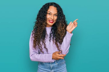 Kış süveteri giyen, kıvırcık saçlı genç İspanyol kadın gülümsüyor. 