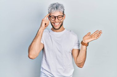 Modern boyalı saçlı, beyaz tişörtlü, gözlüklü, açık avuç içiyle fotokopi çeken ve alnını işaret eden genç İspanyol bir adam. Bunu bir düşün.. 