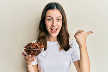 Genç esmer kadın elinde bir kase yıldız anason parmağıyla yan tarafı işaret ediyor mutlu bir şekilde gülümsüyor. 