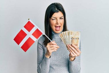 Danimarka bayrağı ve Krone banknotları tutan genç İspanyol kadın kameraya seksi bir ifadeyle bakıyor, neşeli ve mutlu bir yüzle.. 