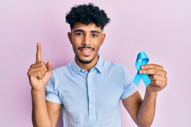Genç Arap yakışıklı adam elinde mavi kurdele ile gülümsüyor bir fikirle ya da soru işareti yaparak mutlu bir yüzle, bir numara 