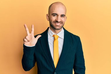 Genç İspanyol bir adam iş elbisesi ve kravat takıyor. Üç numaralı parmaklarıyla işaret ediyor ve gülümsüyor. Kendinden emin ve mutlu.. 