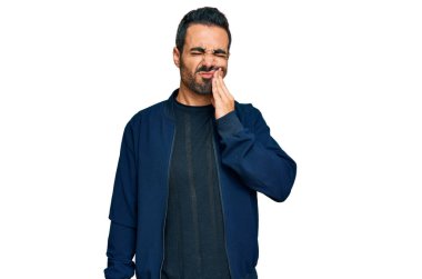 Günlük kıyafetler giyen genç İspanyol adam diş ağrısı ya da diş hastalığından dolayı acı dolu bir ifadeyle ağıza dokunuyor. dişçi 