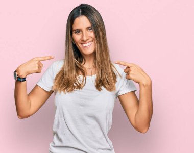 Gündelik beyaz tişört giyen, kendine güvenen, yüzünde gülümseme olan, kendini gururlu ve mutlu gösteren genç bir kadın.. 