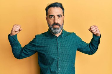 Orta yaşlı, sakallı, gri saçlı, iş kıyafetleri giyen, gururla gülümseyen kol kasları gösteren bir adam. fitness konsepti. 