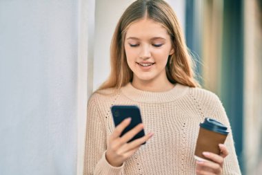 Akıllı telefon kullanan ve şehirde kahve içen güzel beyaz bir genç..