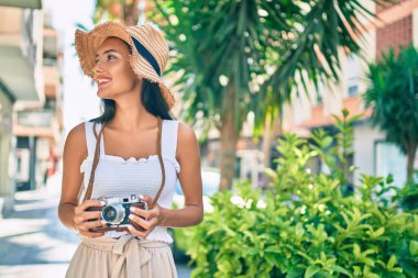 Genç Latin turist kız gülümsüyor. Şehrin caddesinde yürüyen klasik kamera kullanıyor..
