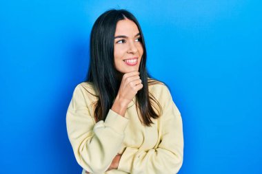 Genç esmer kadın, elleri çenesinde sıradan bir kazak giyiyor ve soru soruyor. Düşünceli bir ifade. Düşünceli bir yüzle gülümsüyor. şüphe kavramı. 