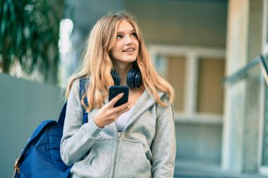 Güzel beyaz öğrenci üniversitede akıllı telefon kullanarak mutlu gülümsüyor..