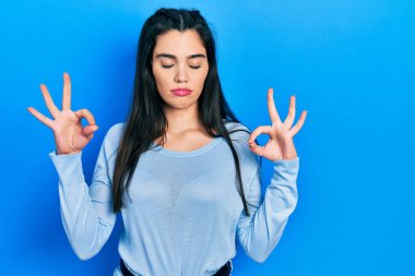 Gündelik kıyafetler giyen, gözleri kapalı gülümseyen genç İspanyol kız parmaklarıyla meditasyon hareketi yapıyor. yoga konsepti. 