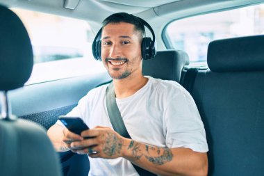 Arabada oturan akıllı telefon ve kulaklık kullanan genç bir İspanyol..