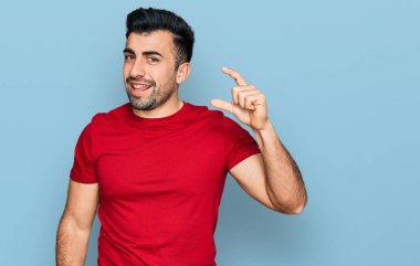 Sakallı, sıradan kırmızı tişörtlü, gülümseyen, kendine güvenen, el hareketi yapan, parmaklarıyla işaret eden ve kameraya bakan İspanyol bir adam. ölçüm kavramı. 