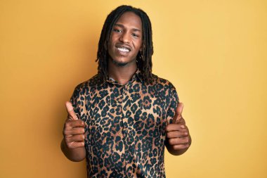 Örgülü, leopar desenli hayvan desenli tişört giyen Afro-Amerikan bir adam. Elleriyle olumlu jest yapıyor. Gülümsüyor ve mutlu. Neşeli ifade ve kazanan jest. 