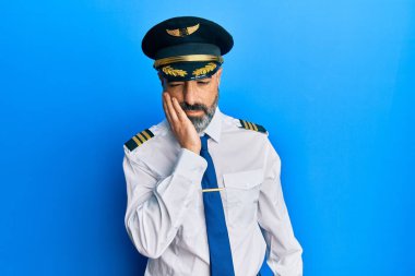 Sakallı, gri saçlı, uçak pilotu üniforması giyen orta yaşlı bir adam çapraz kollu depresyondan sıkılmış ve yorgun göründüğünü düşünüyor.. 