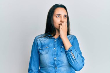 Günlük kot ceket giyen genç İspanyol kadın gergin ve gergin görünüyor. Ağzı tırnak yiyen ellerle. anksiyete. 