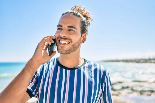 Genç İspanyol gülümseyen adam sahilde akıllı telefondan konuşarak mutlu oluyor..
