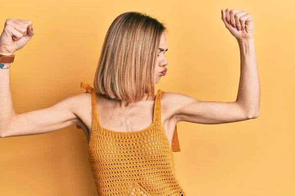 年轻的高加索金发女人穿着休闲的黄色T恤 露出胳膊肌肉 露出自豪的笑容 健身概念 — 图库照片