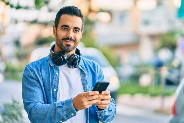 Young hispanic man smiling happy using smartphone and headphones at the city.