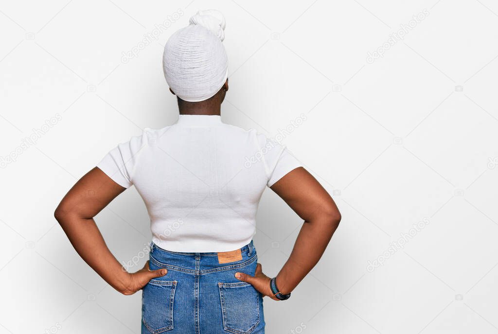 Young african woman with turban wearing hair turban over isolated background standing backwards looking away with arms on body 