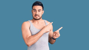 Mayolu ve kolsuz tişörtlü genç yakışıklı bir adam endişeli ve gergin olduğunu gösteriyor. Endişeli ve şaşırmış bir ifade. 