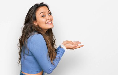 Latin asıllı genç bir kız, gündelik giysiler içinde avuçlarını açıp fotokopi alanını gösteriyor, gülümseyerek mutlu bir şekilde gülümsüyor. 