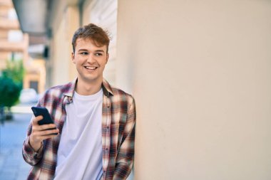 Beyaz adam şehirde akıllı telefon kullanarak mutlu bir şekilde gülümsüyor..