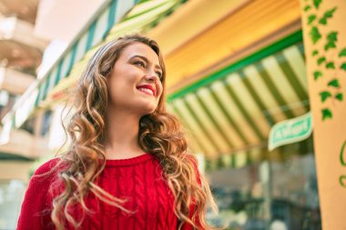 Genç sarışın kız gülümseyerek şehirde mutlu mesut yürüyor..