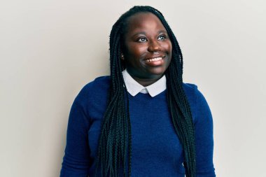 Saçları örgülü genç siyahi bir kadın, rahat bir görünüm takınıyor, rahat bir yüz ifadesi ve kendine güvenen bir gülümseme takınıyor.. 