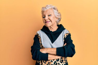 Spor kıyafetleri giymiş, kollarını kavuşturup kameraya gülümseyen yaşlı, gri saçlı bir kadın. pozitif kişi. 