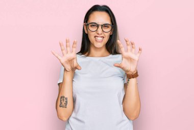 Gündelik beyaz tişört giyen genç İspanyol kadın komik bir şekilde gülüyor kedi gibi pençe hareketi yapıyor, agresif ve seksi bir ifade. 