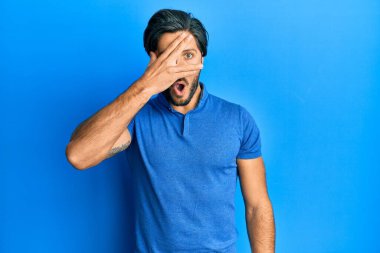 Günlük mavi tişört giyen genç İspanyol adam şok içinde yüzünü ve gözlerini kapayarak parmaklarından korkuyla bakıyor. 