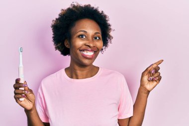 Genç Afro-Amerikalı kadın elinde elektrikli diş fırçası, gülümsüyor. 