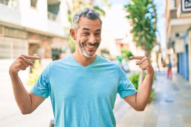 Orta yaşlı, gri saçlı, günlük kıyafetler giyen, kendine güvenen, yüzünde gülümseme olan, kendini gururlu ve mutlu gösteren bir adam.. 