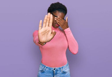 Genç Afro-Amerikalı kız günlük kıyafetler ve gözlük takıyor, gözleri ellerle örtüyor ve üzgün ve korku ifadeleriyle jestleri durduruyor. utangaç ve olumsuz kavram. 