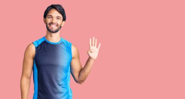 Yakışıklı İspanyol adam spor giyer ve dört numarayı gösterip işaret ederken kendine güvenen ve mutlu bir şekilde gülümser.. 